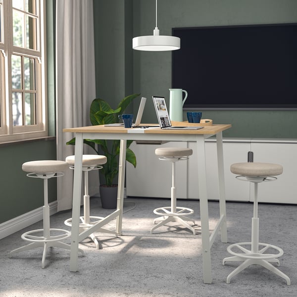 Modern conference table with 4 white stools, light wood top, metal legs, cable management, adjustable footrests, large window, tv, tableware.