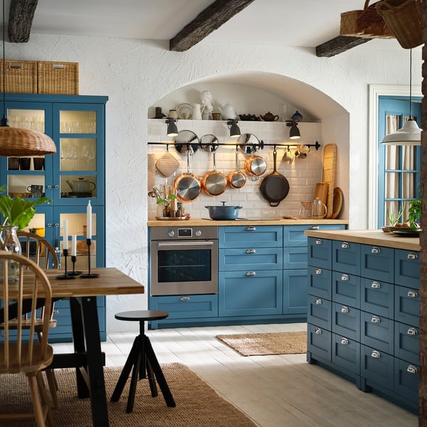 Well-organized kitchen with blue cabinets, wooden countertops, hanging pots, and modern appliances.