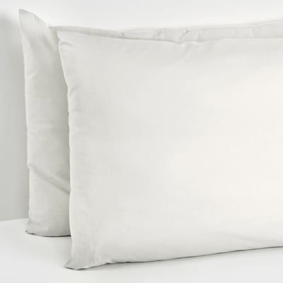 Two white pillows are stacked neatly, with one lying flat and the other leaning against a wall, providing comfort and support for a cosy setting.