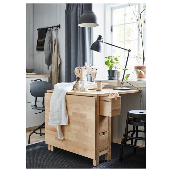 Minimalist craft room with light wood desk, sewing machine, black stool, and adjustable lamp.