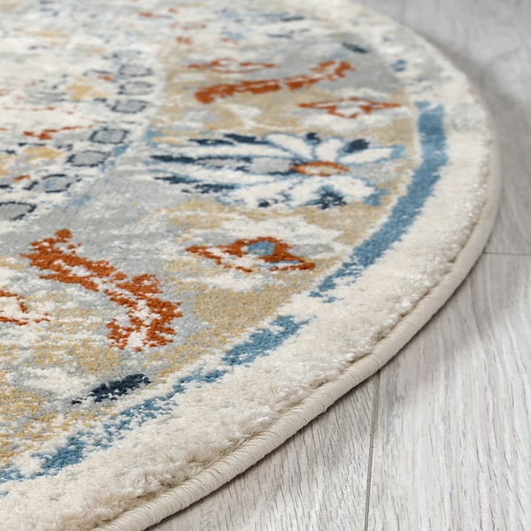 Round decorative rug with faded oriental patterns, placed on a light wooden floor.