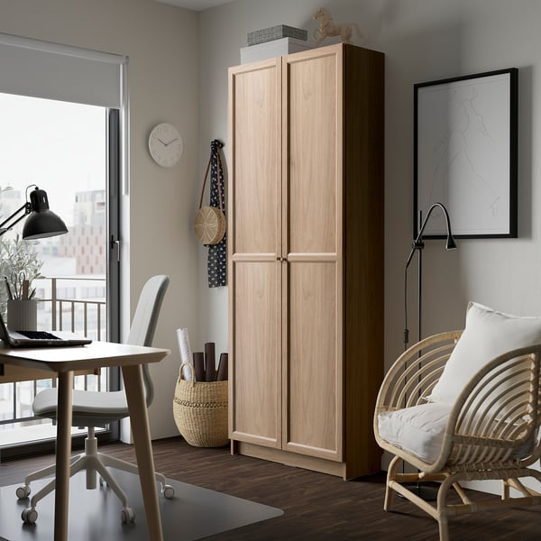 Tall wooden OXBERG bookcase in light colour between desk and chair, fits well in room.