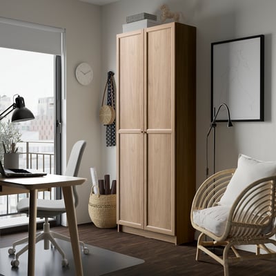 Tall wooden OXBERG bookcase in light colour between desk and chair, fits well in room.