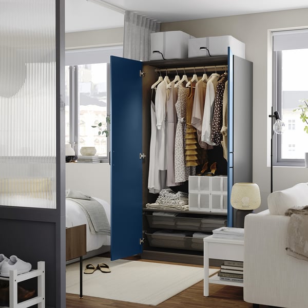 Modern bedroom featuring a blue PAX wardrobe with clothes and accessories neatly organised inside.