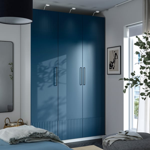 Modern bedroom with blue PAX wardrobe, reflective doors, bed, and tall lamp.