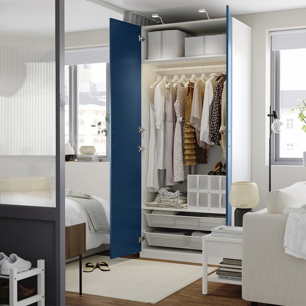 A modern bedroom with a blue-patterned PAX wardrobe open, revealing clothing and shelves. The wardrobes organisation and interior design.