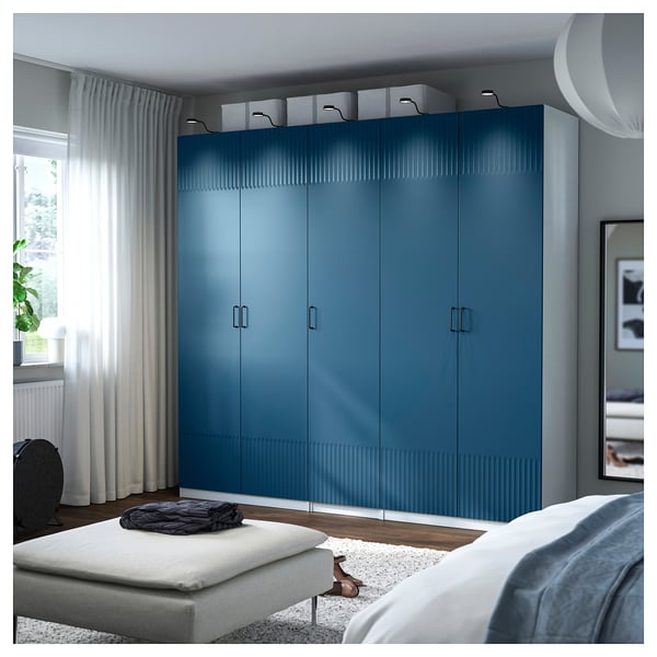 Blue PAX wardrobe in bedroom, larger than bed, with multiple drawers and shelves.