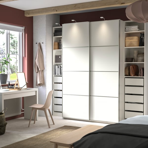 Modern bedroom with white PAX wardrobe, sliding doors, and organised shelves. Neutral decor with a desk and chair, natural light from window.
