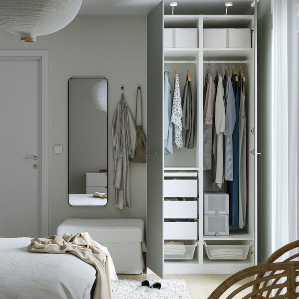 Bedroom with a large PAX wardrobe, neatly organised with clothes hangers and storage drawers. A mirror and bench are placed alongside the wardrobe.