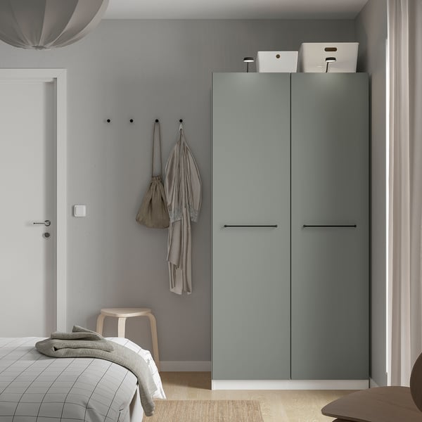 Modern grey PAX wardrobe with storage boxes, hanging items, and stool. Tall, sleek design.