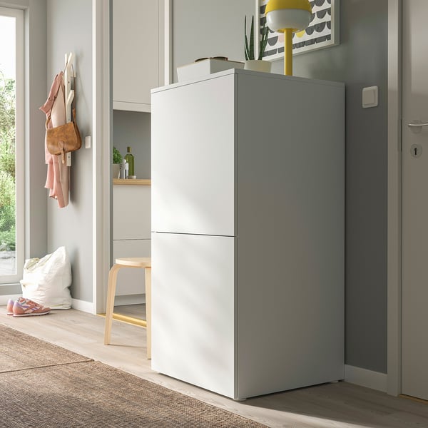 Modern grey PLATSA cabinet in entryway. Tall, rectangular, with sleek white handles. Accompanied by coats, shoes, and stools.