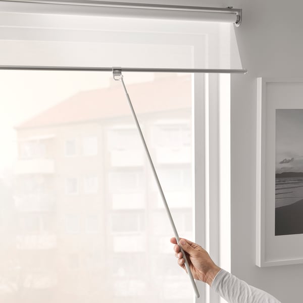 Pulling white roller blind with extendable draw rod on window.
