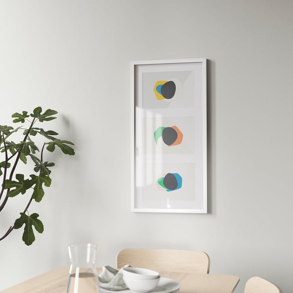 A modern frame with colourful art on a grey wall, a wooden table with cups and a glass, and a green plant.