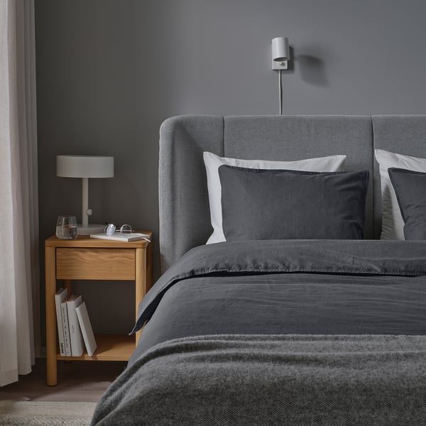 A modern bedroom with a grey duvet, padded headboard, bedside table, and lamp. Minimalist design emphasises simplicity and comfort.