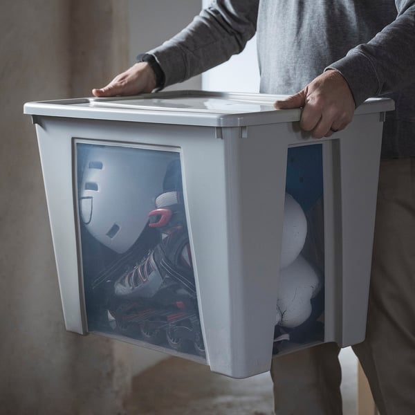 Person carrying large white SAMLA storage box, visible contents inside through transparent windows.