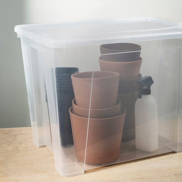 A clear plastic storage box holding stacks of clay pots and a spray bottle.
