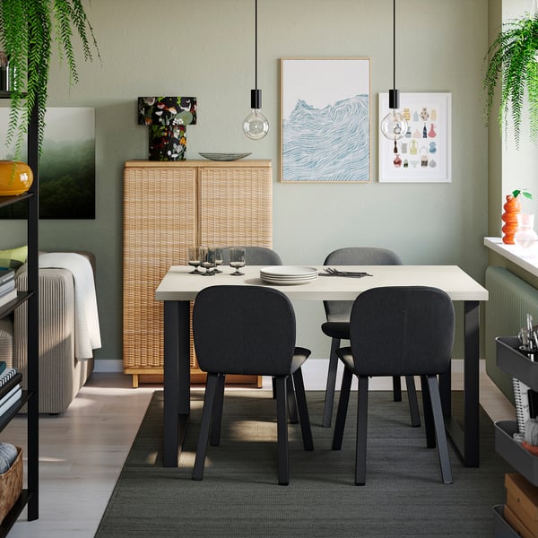 A modern dining room with SKÅLSTA table, grey chairs, white settings, photos, lights, and a green rug. Minimalist and inviting.