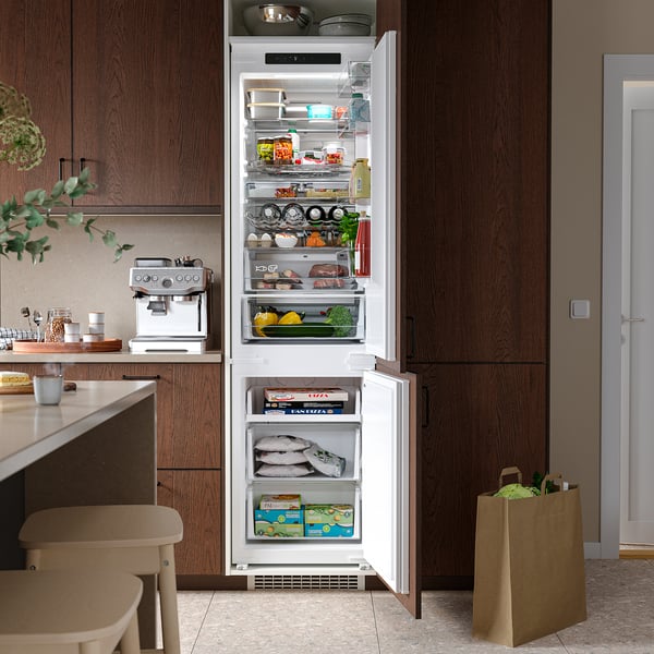 Open integrated fridge/freezer reveals shelves with various groceries, highlighting its spacious interior and organised storage.