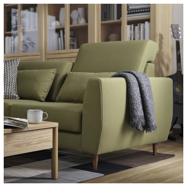 Olive green SLATORP sofa with wooden legs, dark throw blanket, coffee cup, and geometric rug, cosy modern living room setup.