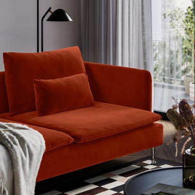 Bright orange SÖDERHAMN sofa with two pillows, black lamp, and chequered rug in modern living room by large window.