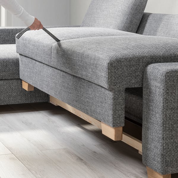 Person opening storage under modern grey sofa with wooden legs.