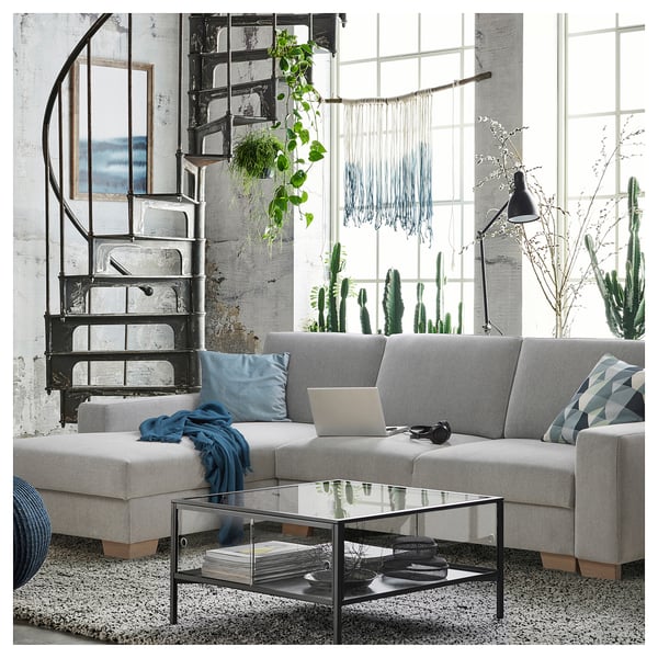 Modern living room with grey SÖRVALLEN sectional sofa, glass coffee table, black metal spiral staircase, large windows, and green cacti.