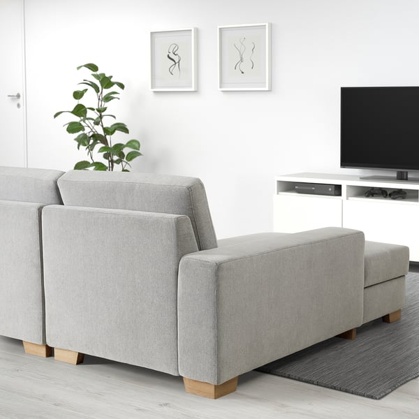 Modern minimalist grey SÖRVALLEN sofa with light wood legs in a living room, accompanied by a small tv stand and plant, with wall art above.
