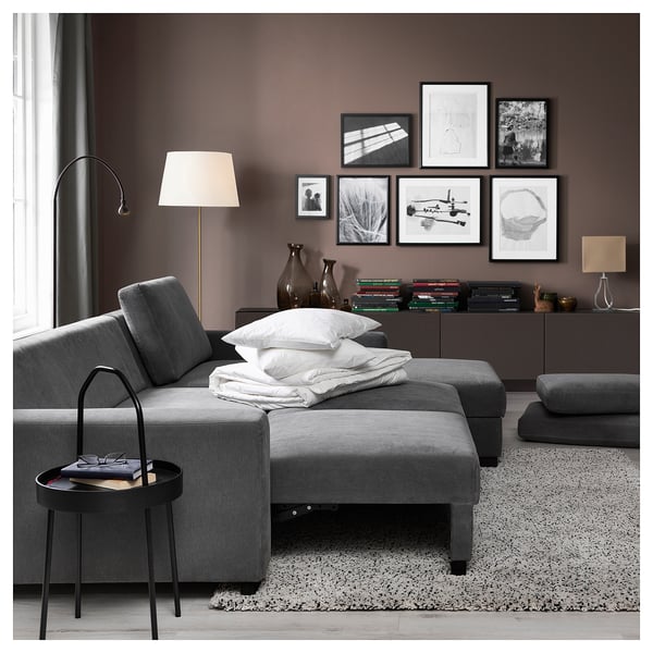 Modern grey sofa with chaise, black side table, floor lamp, and various pillows; cosy living room setup.
