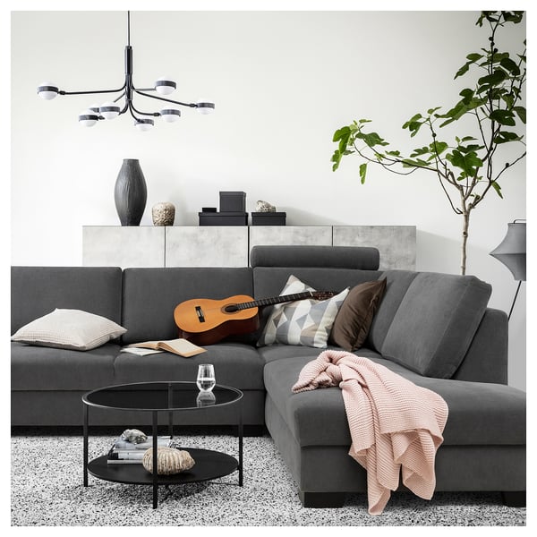 Modern grey sectional sofa with cushions, guitar, glass table, plant, and colourful pillows.