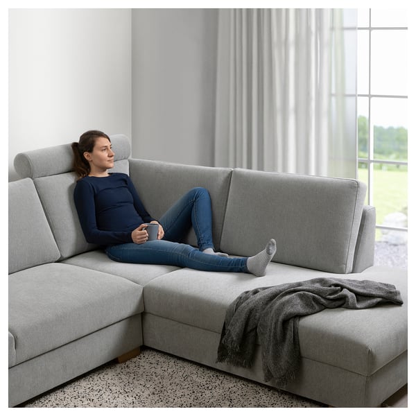 Person relaxes on grey SÖRVALLEN sectional sofa, holding a mug, near large windows with curtains.