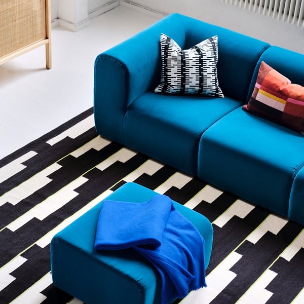 Blue STOCKHOLM 2025 sectional couch with black/white pillows, rug, and blanket in minimalist living room.