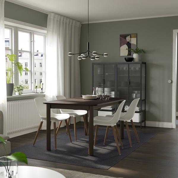Modern dining room with STRANDTORP table and 4 chairs on a blue rug. Green walls, large windows, art, cabinet, and a plant.