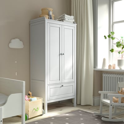 Kids room with grey SUNDVIK wardrobe, crib, & window. Toy box, cloud lamp, rocking chair, & dotted rug.