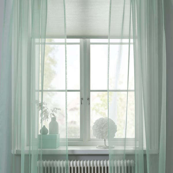 Sheer green curtains by a window, diffusing light and offering privacy. White radiator below, vases on sill.