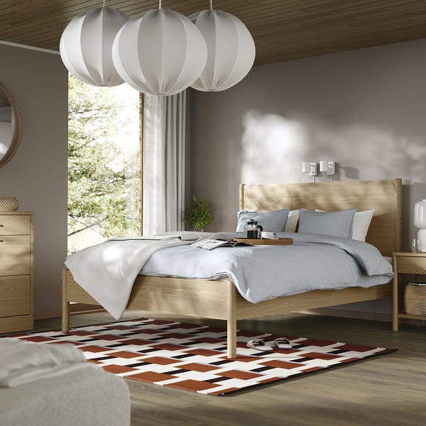 Modern bedroom with TONSTAD light wood bed, white linens. Large window, colourful rug, hanging lamps. Cosy, inviting.