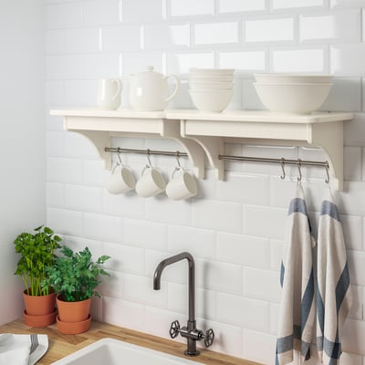 White shelf holds mugs, bowls, and pots; hooks below for hanging towels, kitchen against tiled wall.