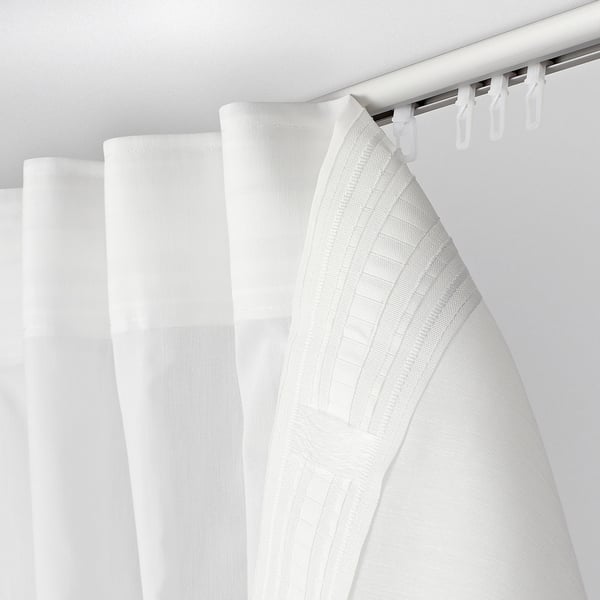 White shower curtain with textured pattern, drawn partially open on hooks.
