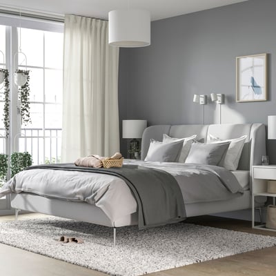 Modern bedroom with TUFJORD bed, rug, nightstands, and plants. Beige curtains frame large window.