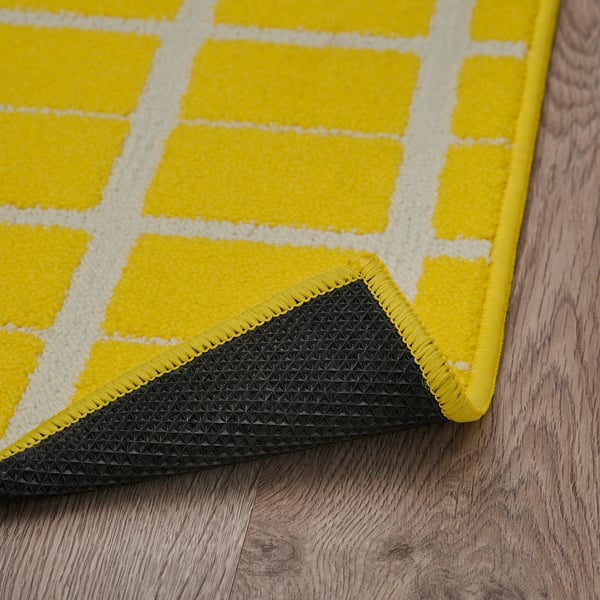 Bright yellowchecked rug with white squares, black non-slip backing, cosy and secure.