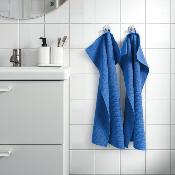 Two blue VÅGSJÖN towels hang on bathroom wall, larger than toiletries on counter.