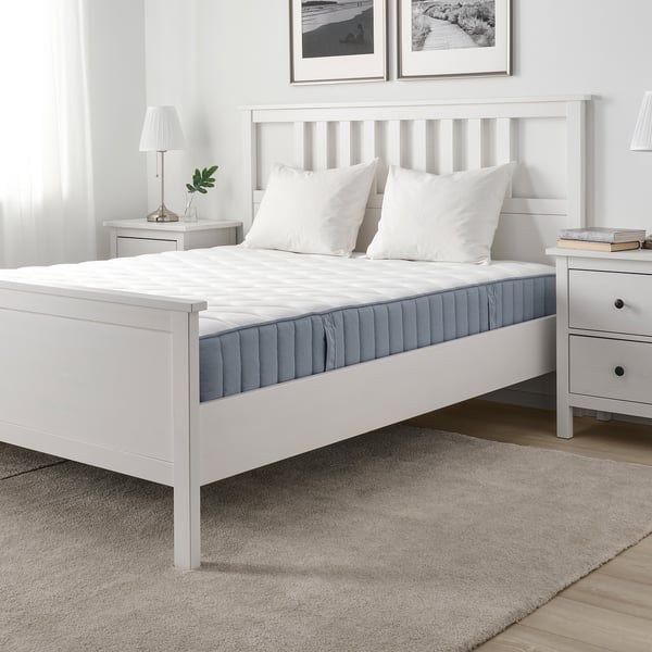 Minimalist bedroom with white VÅGSTRANDA mattress, two pillows, grey rug, wood floor, and black/white art.