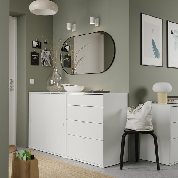 Modern green room with white furniture including a dresser, chair, and stool. Artwork, a mirror, and decorative items.