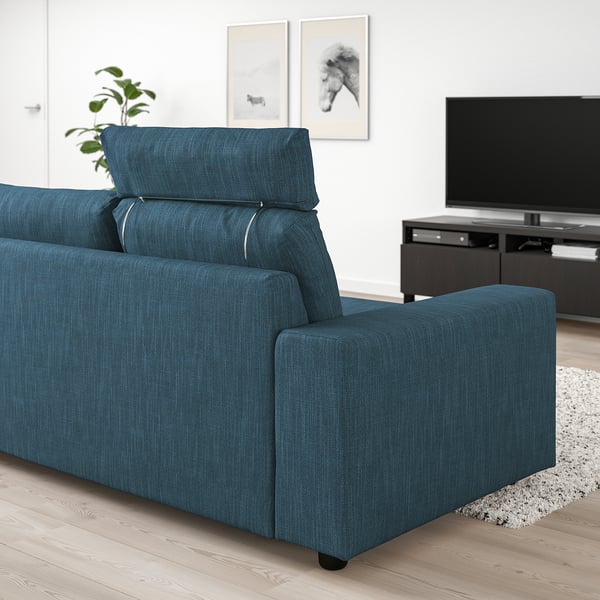 A blue VIMLE sofa with headrests in a living room. Its large, matching a wall-mounted tv and a rug. The design is modern with plush cushions.