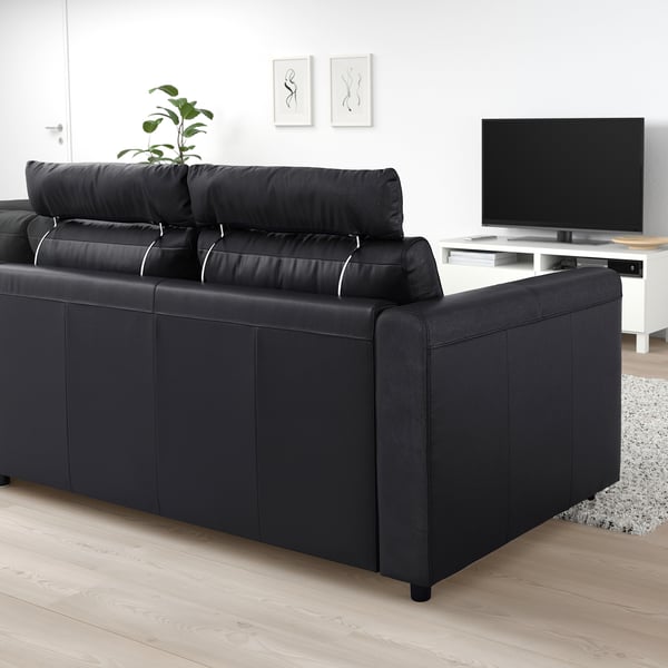Black VIMLE sofa in modern living room. Wide, comfortable design with backrest pillows. Tv and rug nearby, white walls.