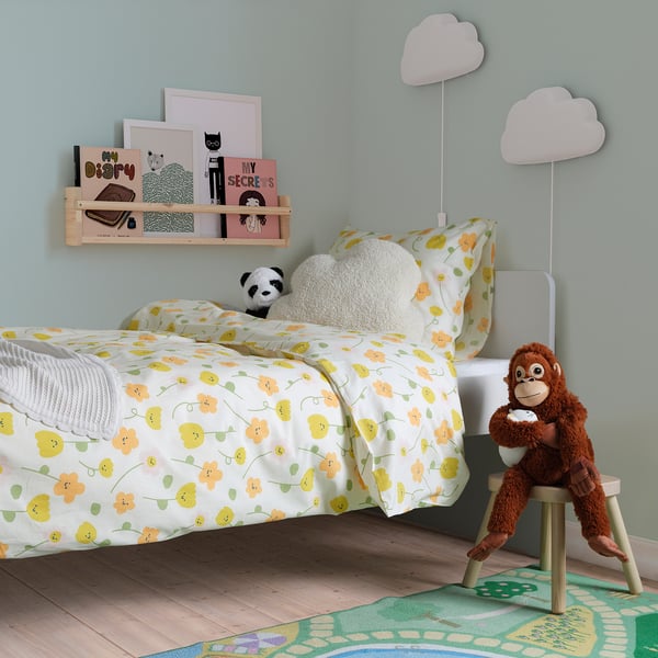 Dětský pokoj s polštářem na obláčku, květinovým povlečením, plyšovou opičkou a knihovnou.