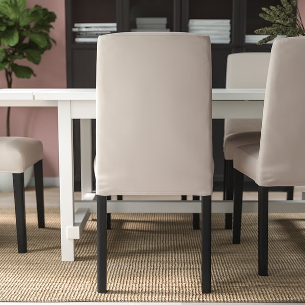 Moderní jídelní uspořádání s čalouněnými židlemi kolem bílého stolu. Židle mají béžové potahy a černé nohy, které nabízejí pohodlí a styl.