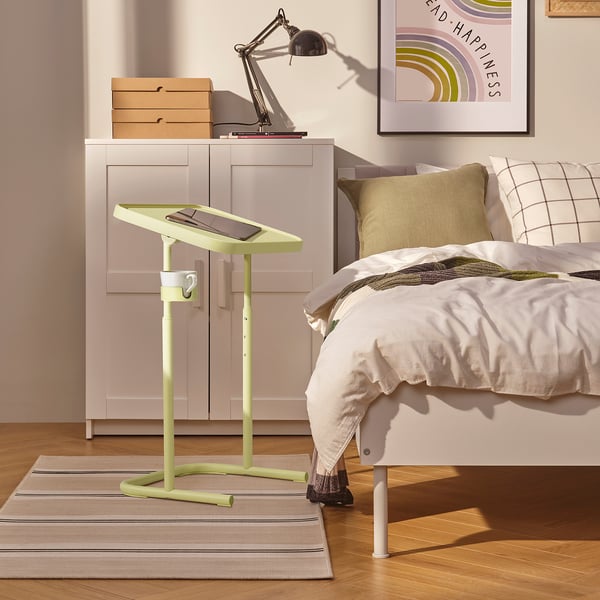 Malý zelený stolek na notebook vedle postele, držící tablet, s nastavitelnou výškou.