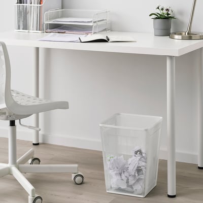 Bílý kovový koš na papír pod stolem vedle židle. Jednoduchý moderní design. Menší než židle a stůl.