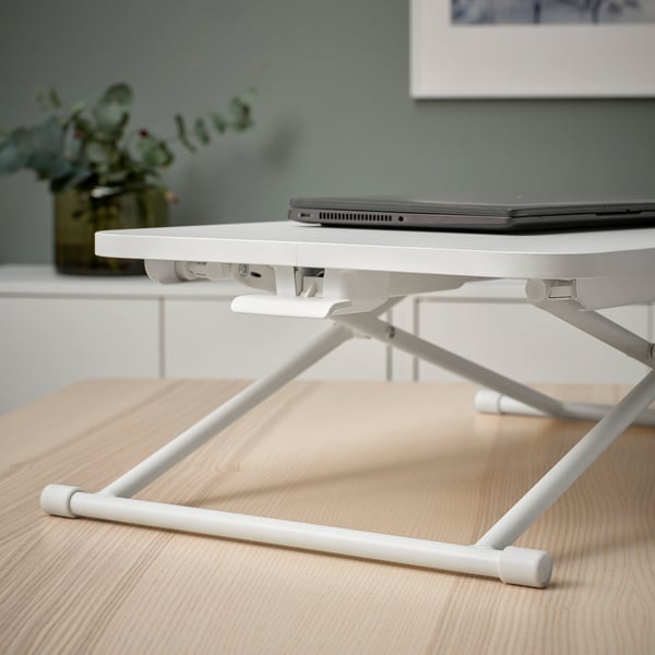 Bílý notebook stojí na dřevěném stole a drží otevřený notebook ve vyvýšené, ergonomické výšce pro pohodlnou práci.