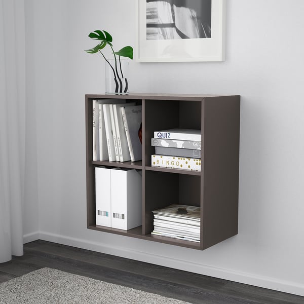 Nástěnná úložná skříň EKET. Na policích má knihy, hry a vázu. Skříň je efektivní pro úsporu místa a organizaci.